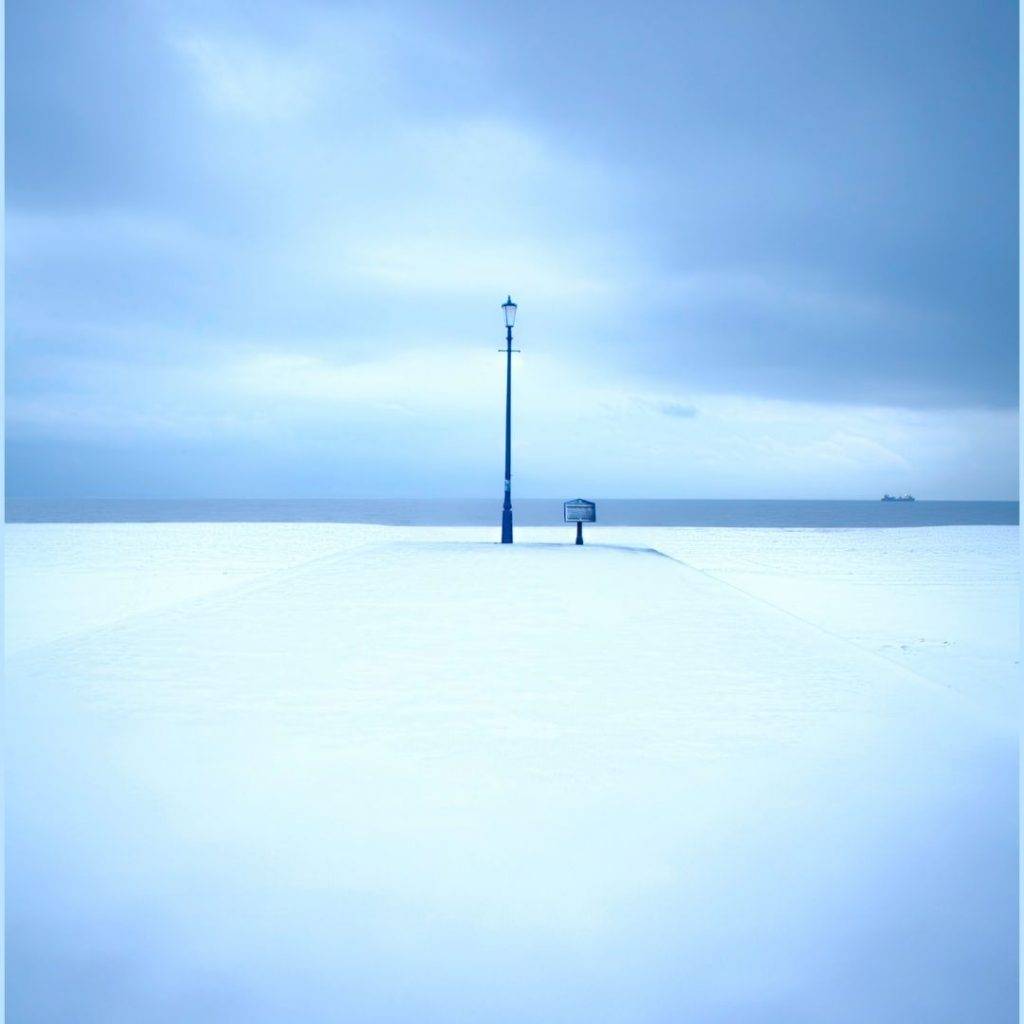 Strassenlaterne und Briefkasten in weisser Winterlandschaft vor dem Meer