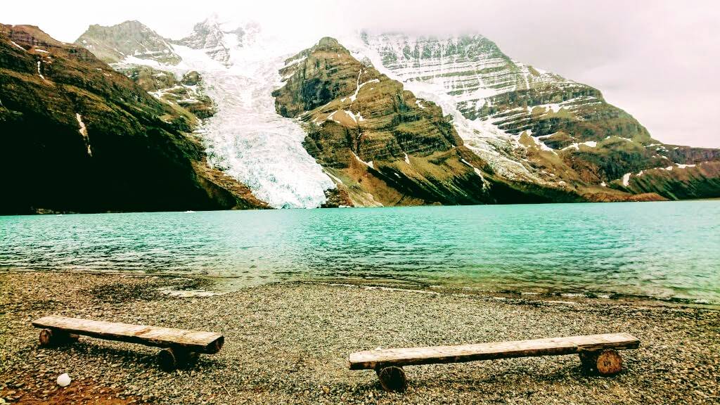 Zwei Holzbaenke auf Steinen vor einem Gletschersee am Mount Robson in British Columbia, Canada.